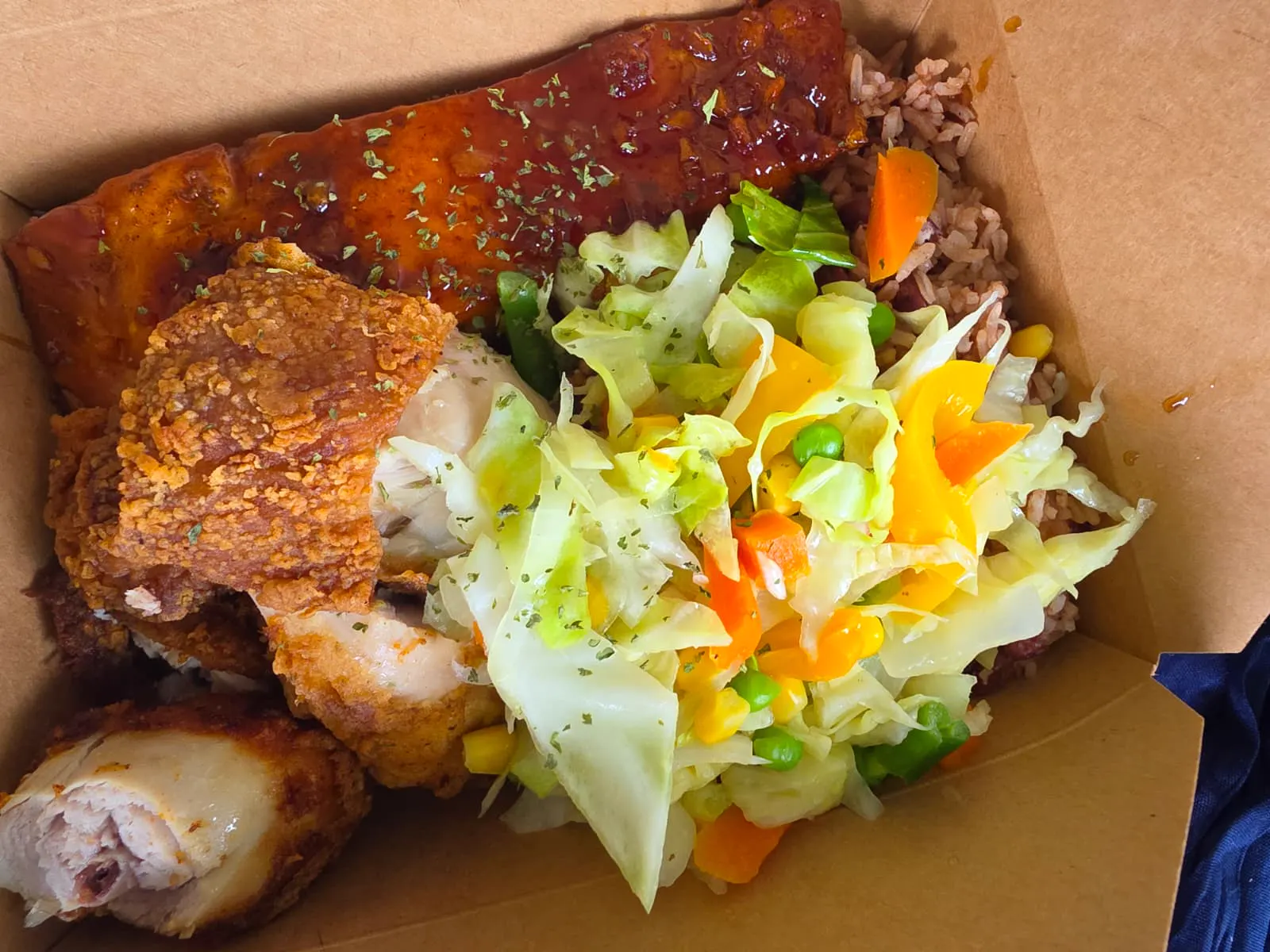 A boxed meal of fried chicken, rice and peas and steamed cabbage