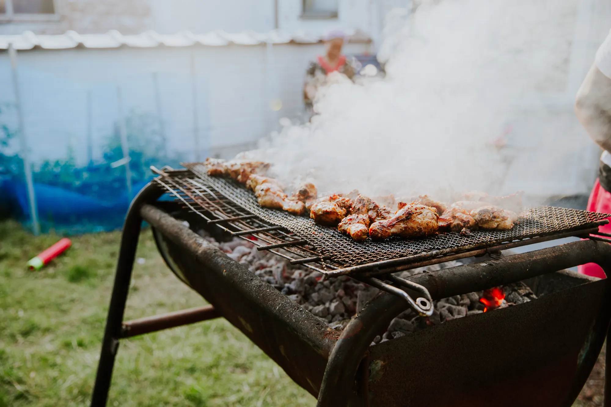 Chicken cooking over a smoking charcoal grill at an outdoor gathering